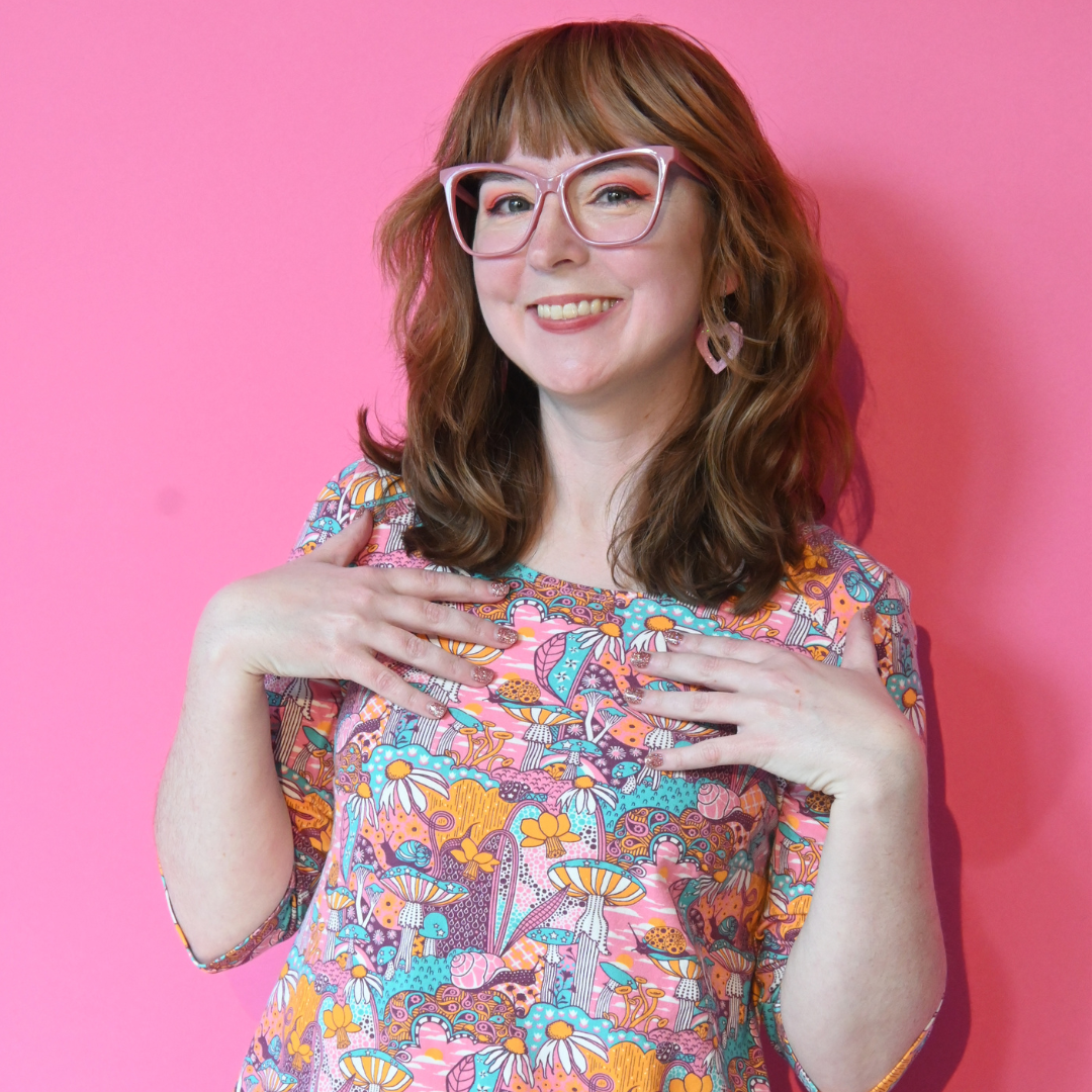Model wearing pink, yellow and aqua pocket tunic with mushrooms, flowers and snails