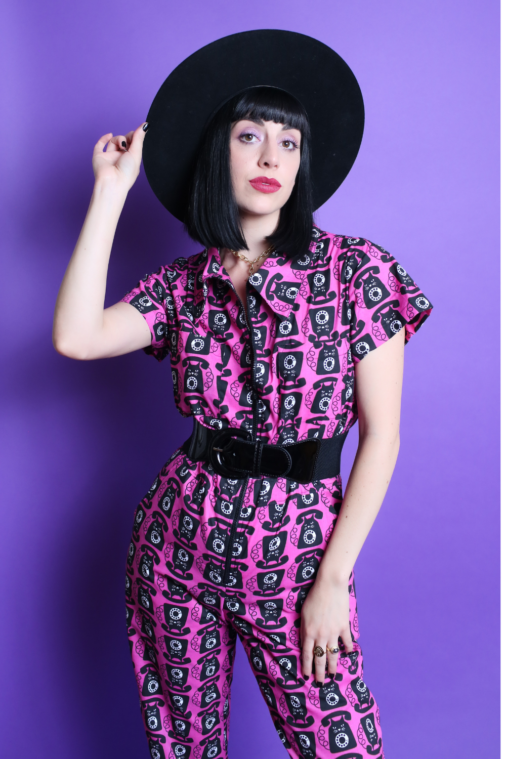 Black haired model in black hat and pink and black printed jumpsuit