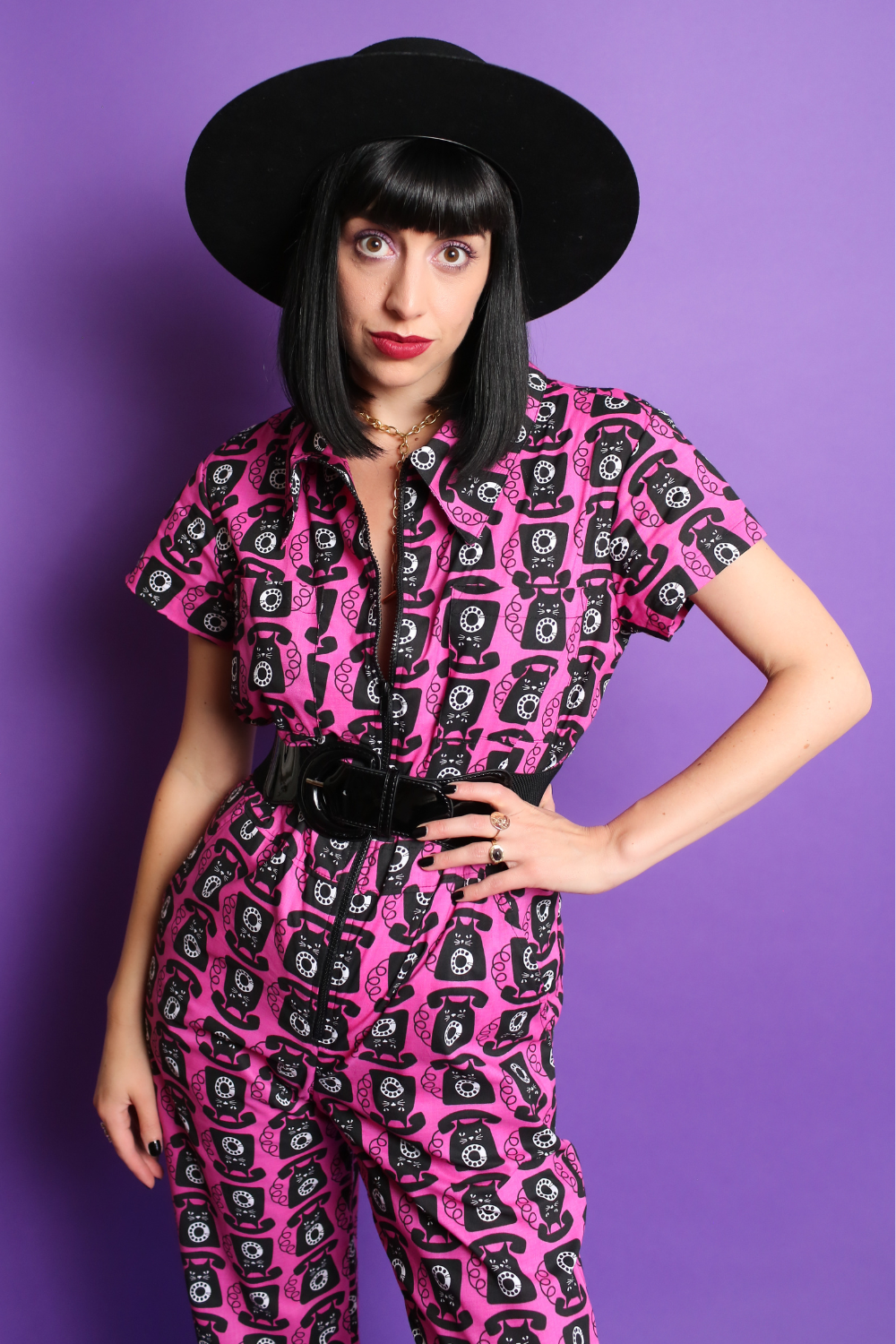 Black haired model in black hat and pink and black printed jumpsuit