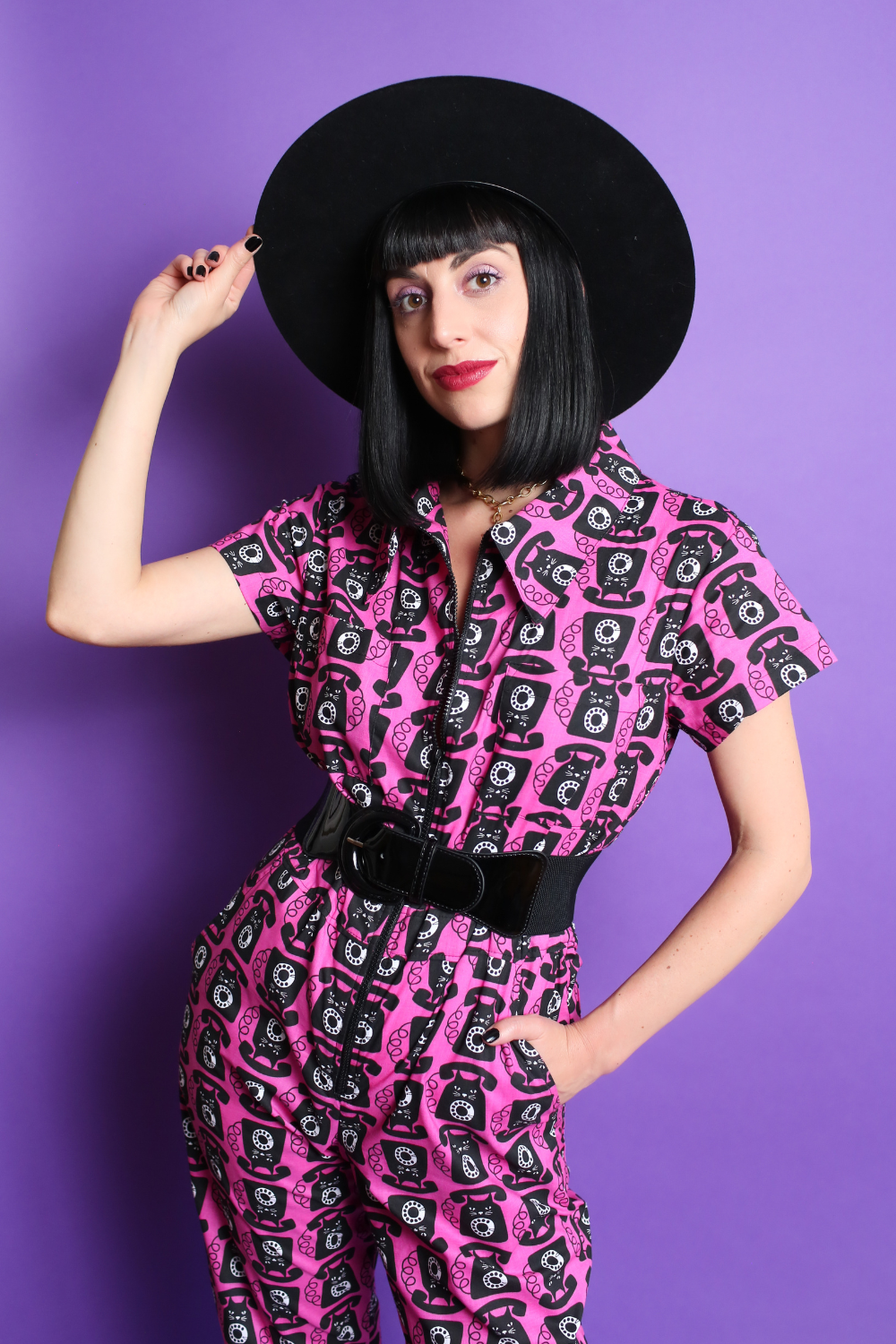 Black haired model in black hat and pink and black printed jumpsuit