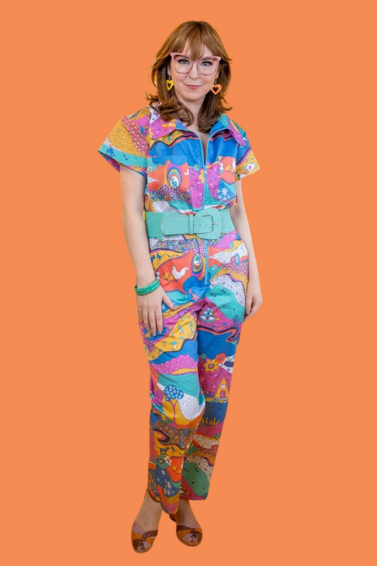 Model wearing glasses and brightly colored printed jumpsuit with zipper and collar