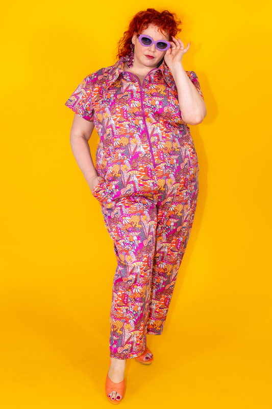 Red-haired model in bright mushroom print jumpsuit and purple sunglasses
