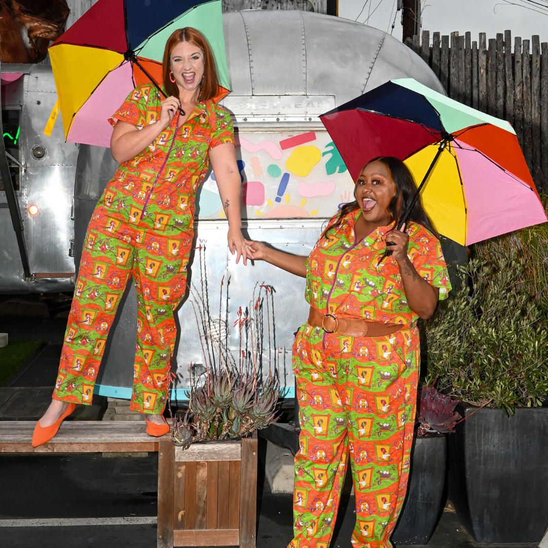 2 girls holding hands and umbrellas, wearing darling coveralls in orange, green and yellow geometric print with ladies and birds nests