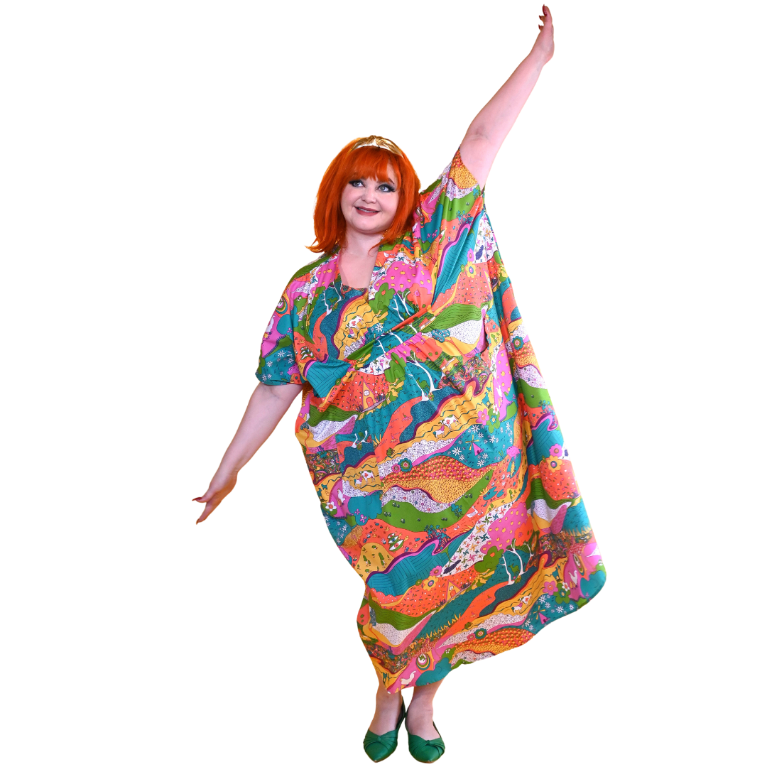 Red-haired model in bright, colorful printed caftan dress, posing with extended arms