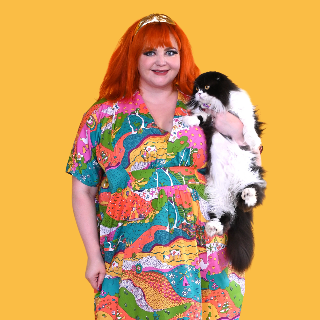 Red-haired model in bright, colorful printed caftan dress holding black and white cat