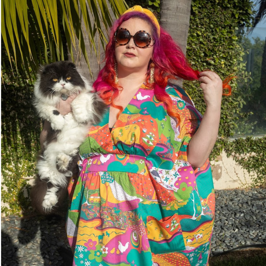 Pink-haired model in bright , colorful caftan, holding cat