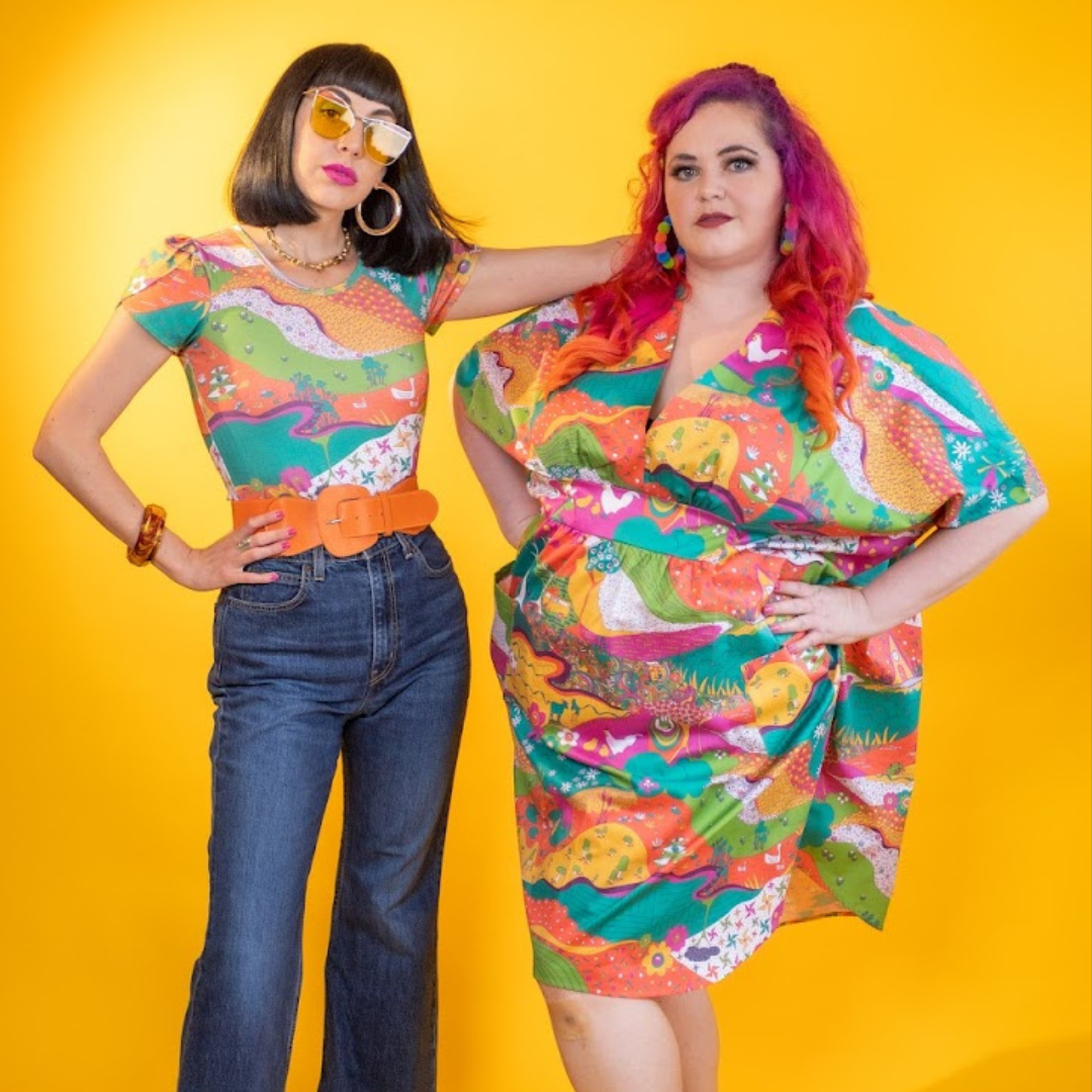 Black-haired model in bright, colorful printed tee and pink-haired model in bright, colorful caftan