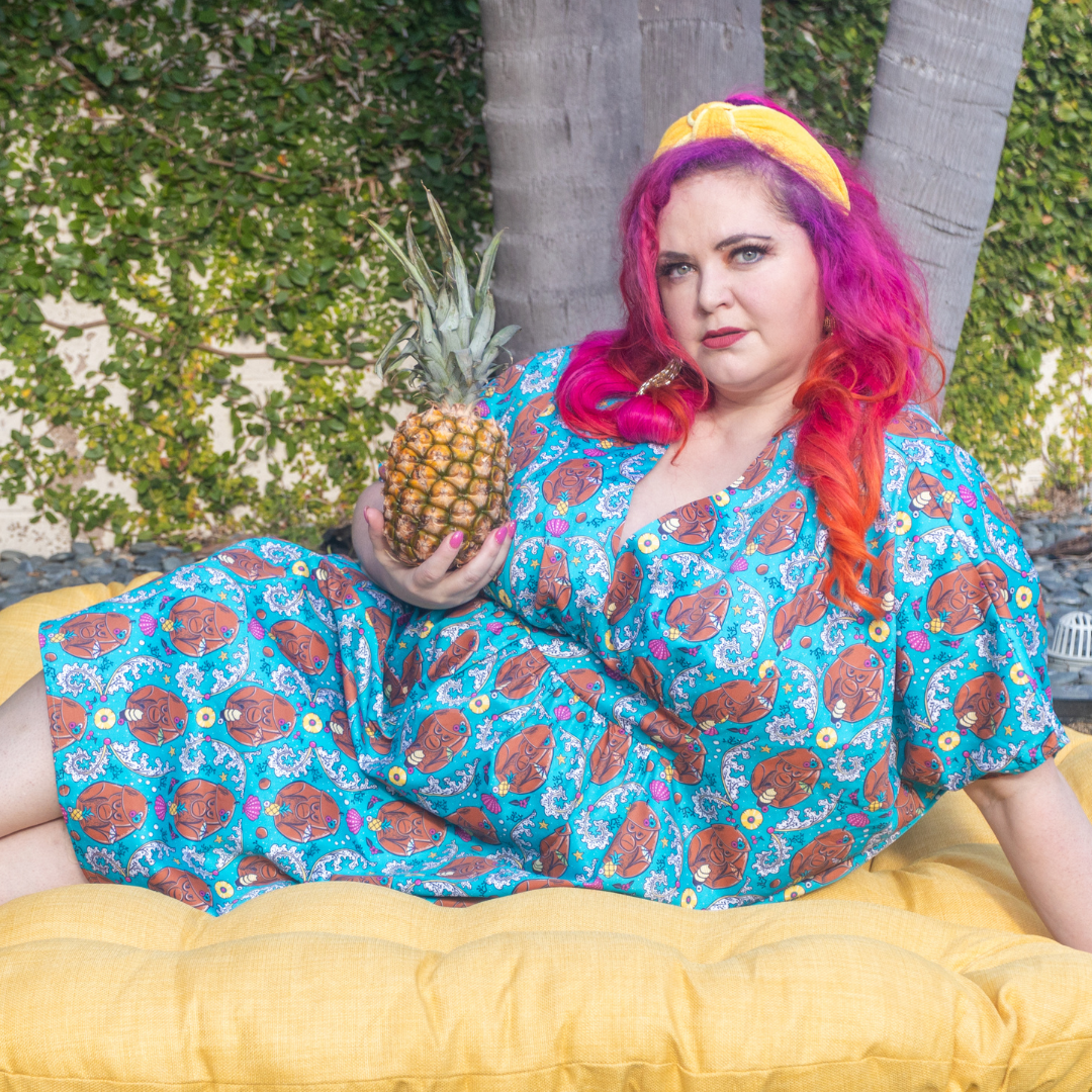 Model with bright hair lounging in teal monkey caftan with pineapple