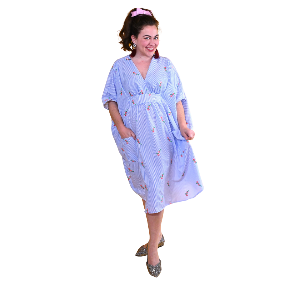 Model smiling and wearing seersucker caftan with floral embroidery