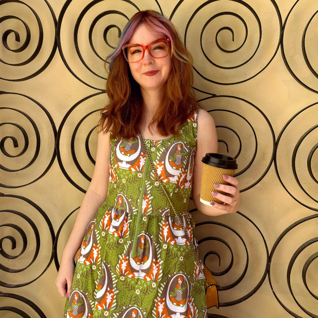 Model in olive green dress with reading girls, foxes and egg chairs, and holding a coffee