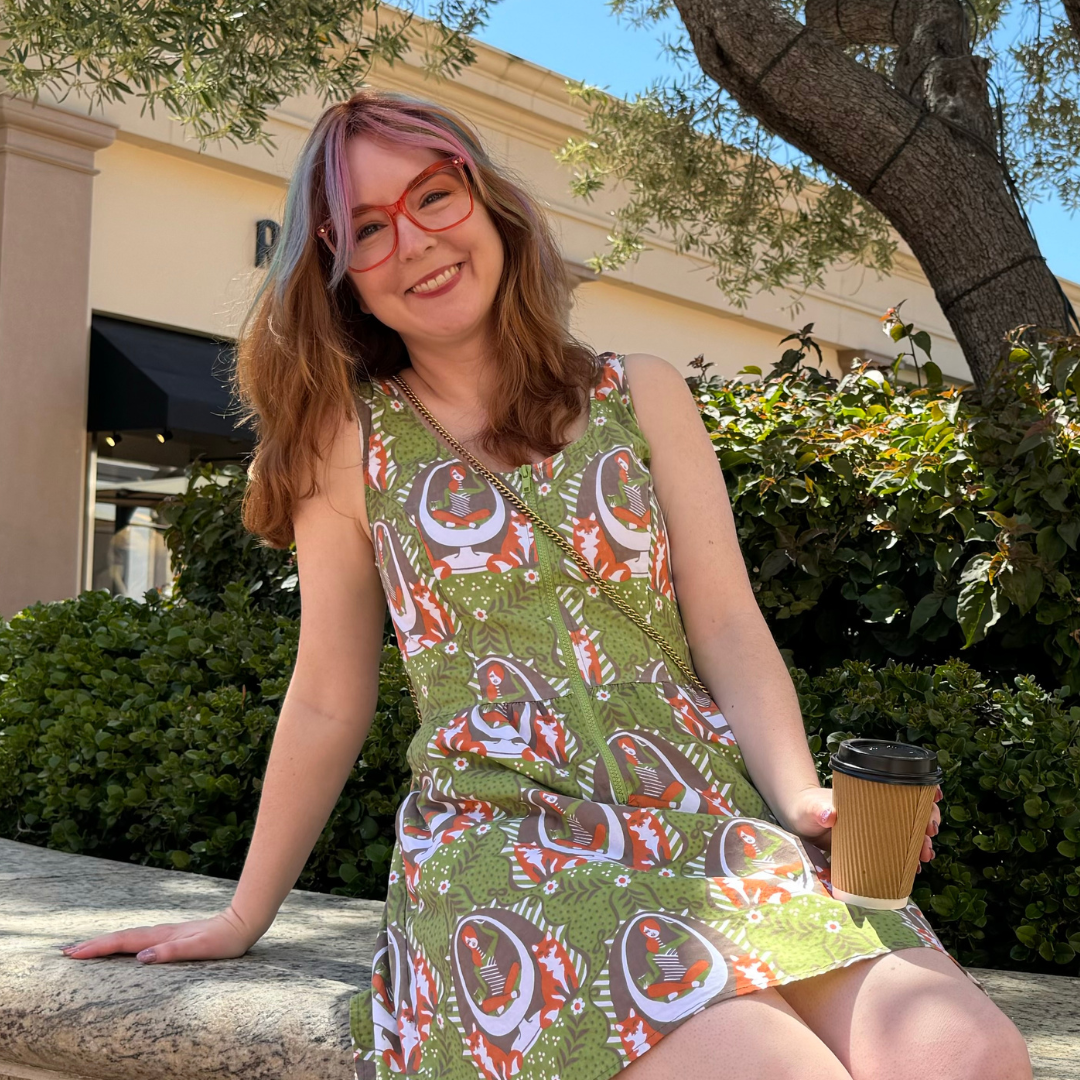 Smiling model in olive green printed dress holding a cup of coffee