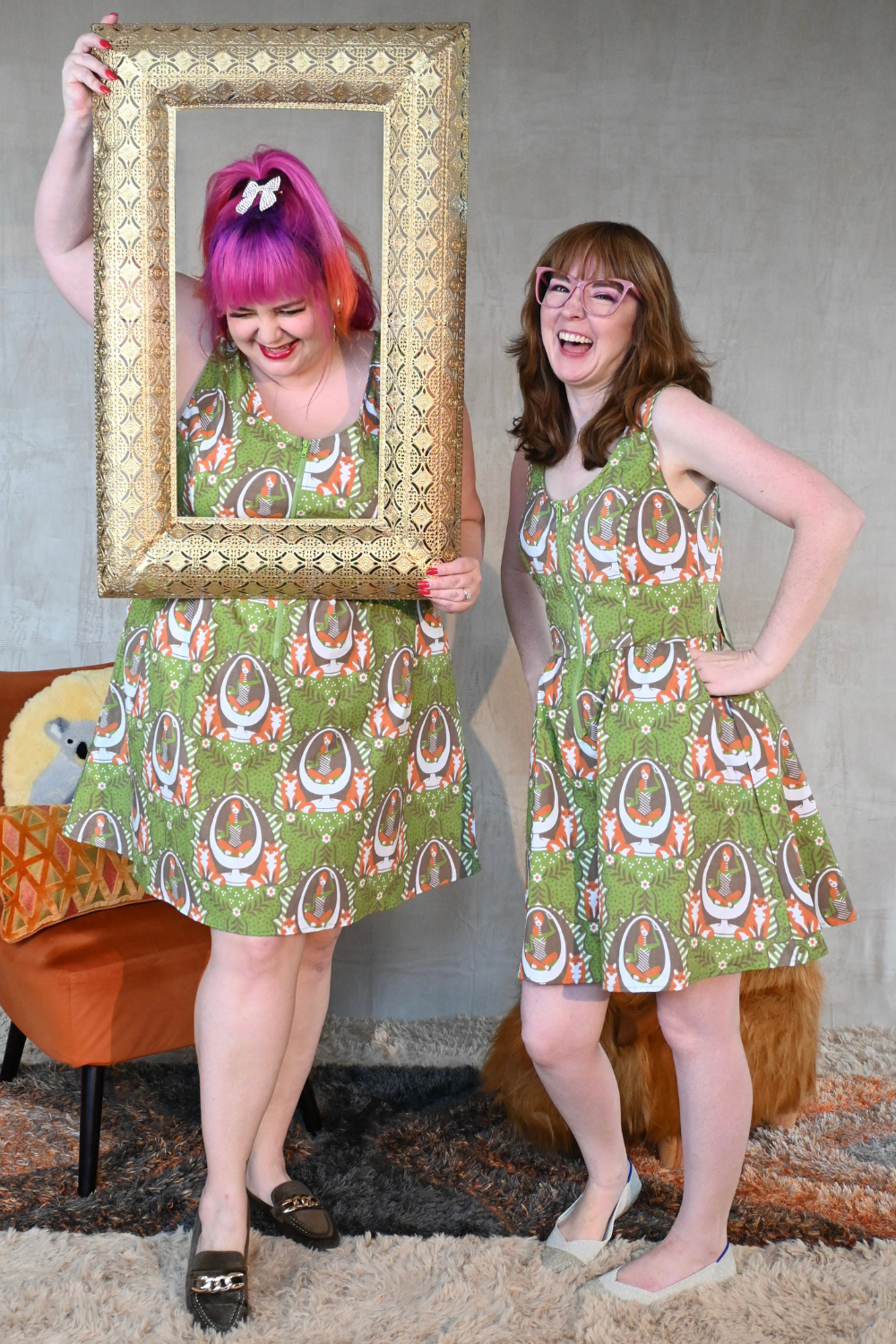 Laughing models in olive green zip-front knee-length dresses in fun print posing with picture frame