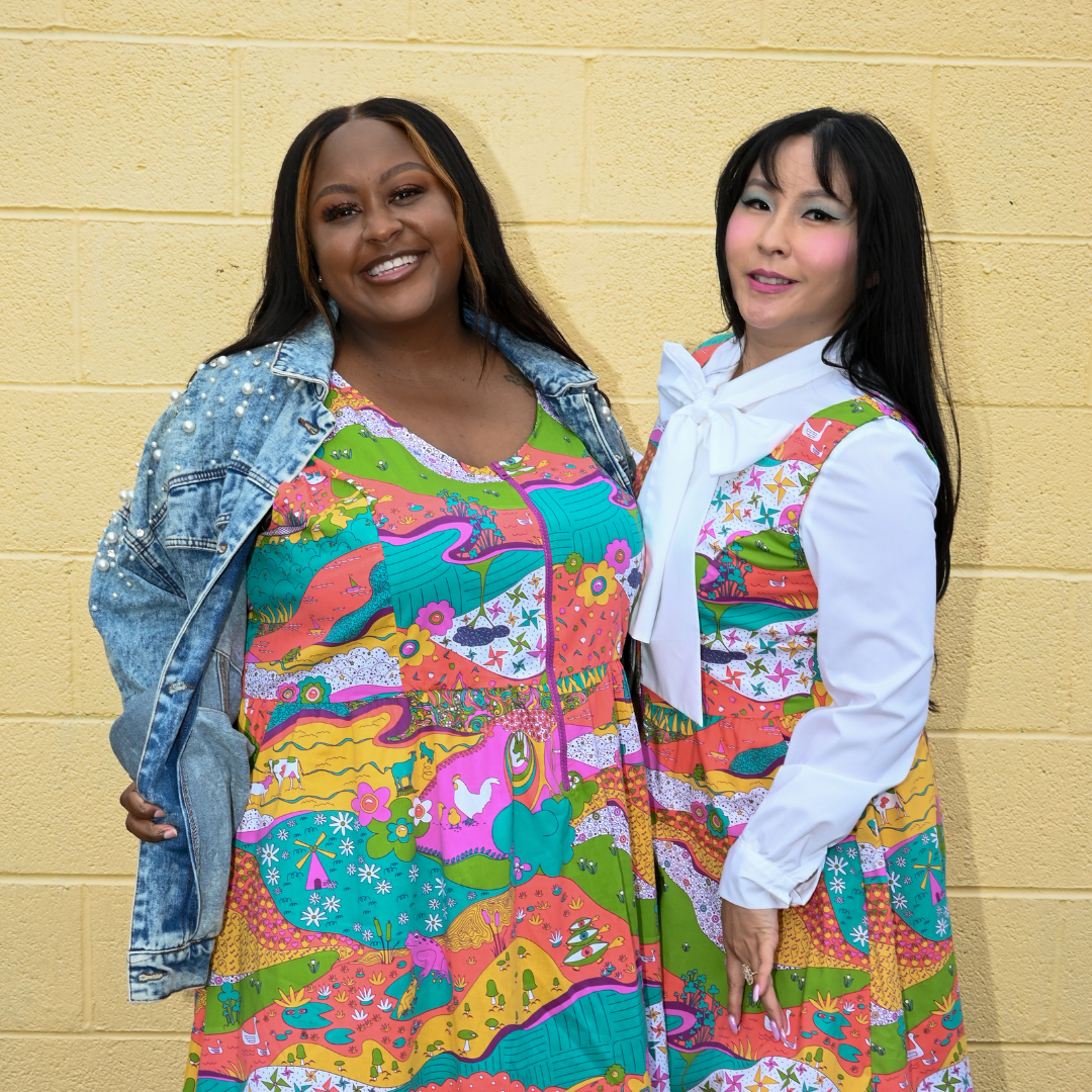 2 pretty girls in matching bold landscape print zip-front dresses, in front of brick wall