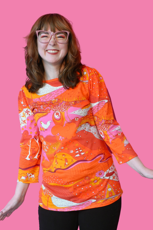 Fun brown-haired girl in pink glasses and bright orange pink red landscape print graphic tee