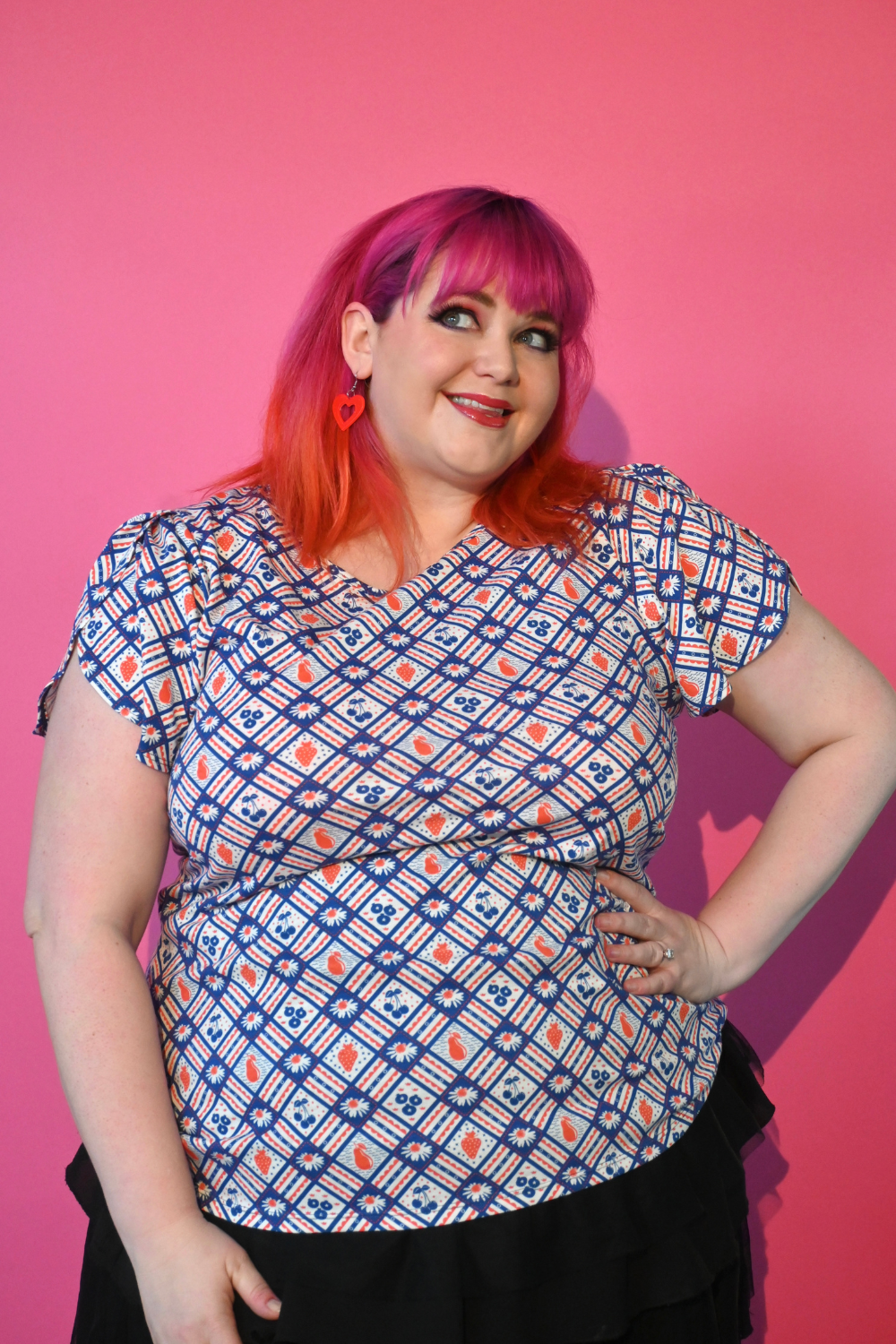 Pink-haired plus size model wearing red and navy fruit and gingham print tee