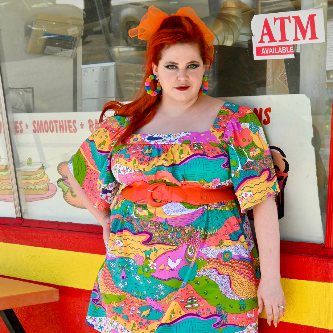 Red-haired model in brightly colored printed dress and fun accessories, in front of donut shop
