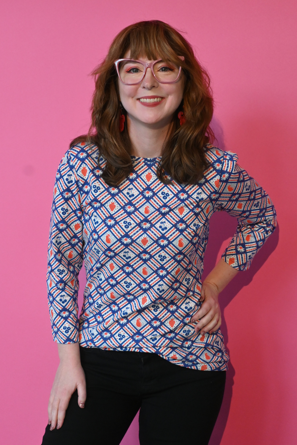 Smiling model wearing glasses and flower and fruit print graphic tee in navy and red