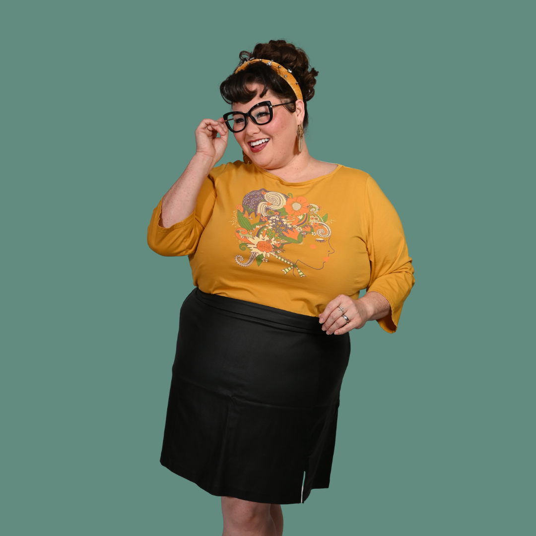 Person wearing a yellow shirt with a colorful design and a black skirt on a green background