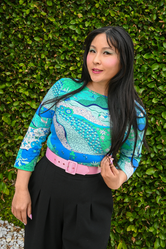 Pretty Asian model posing in blue and green landscape print tee in front of hedge