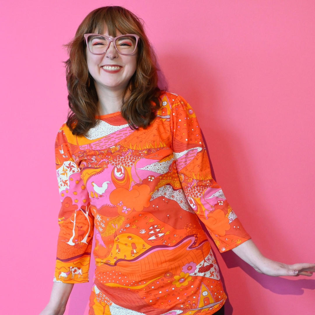 Fun brown-haired girl in pink glasses and bright orange pink red landscape print graphic tee