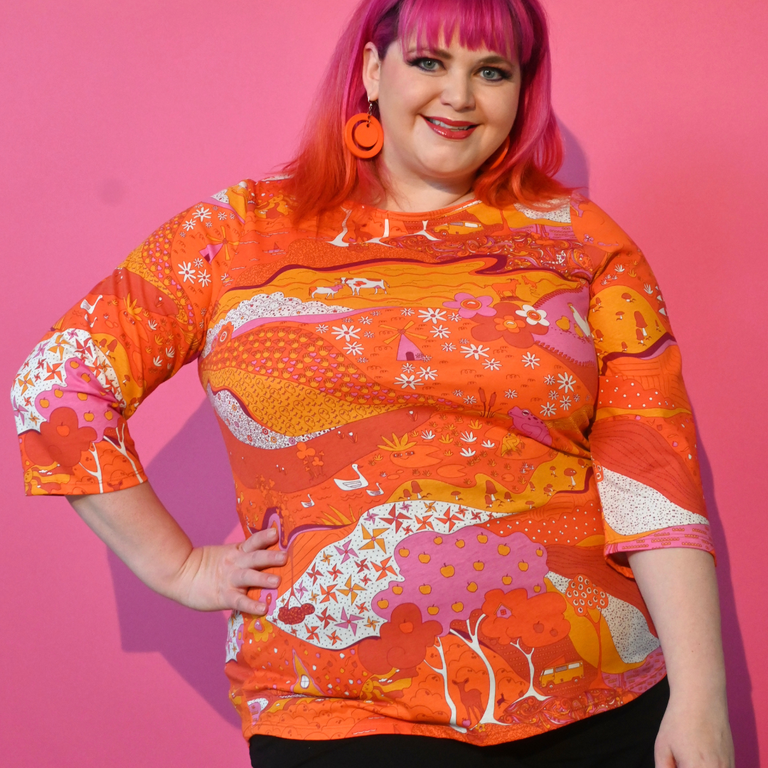 Pink-haired girl wearing orange pink red landscape print graphic tee