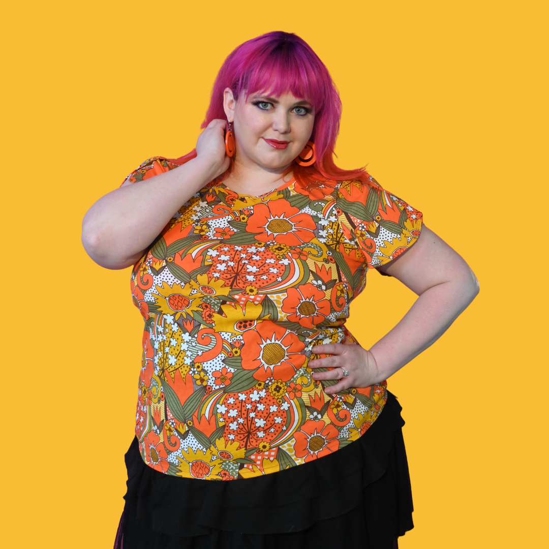 Pink-haired model wearing large earrings and orange, yellow and green flower print t-shirt