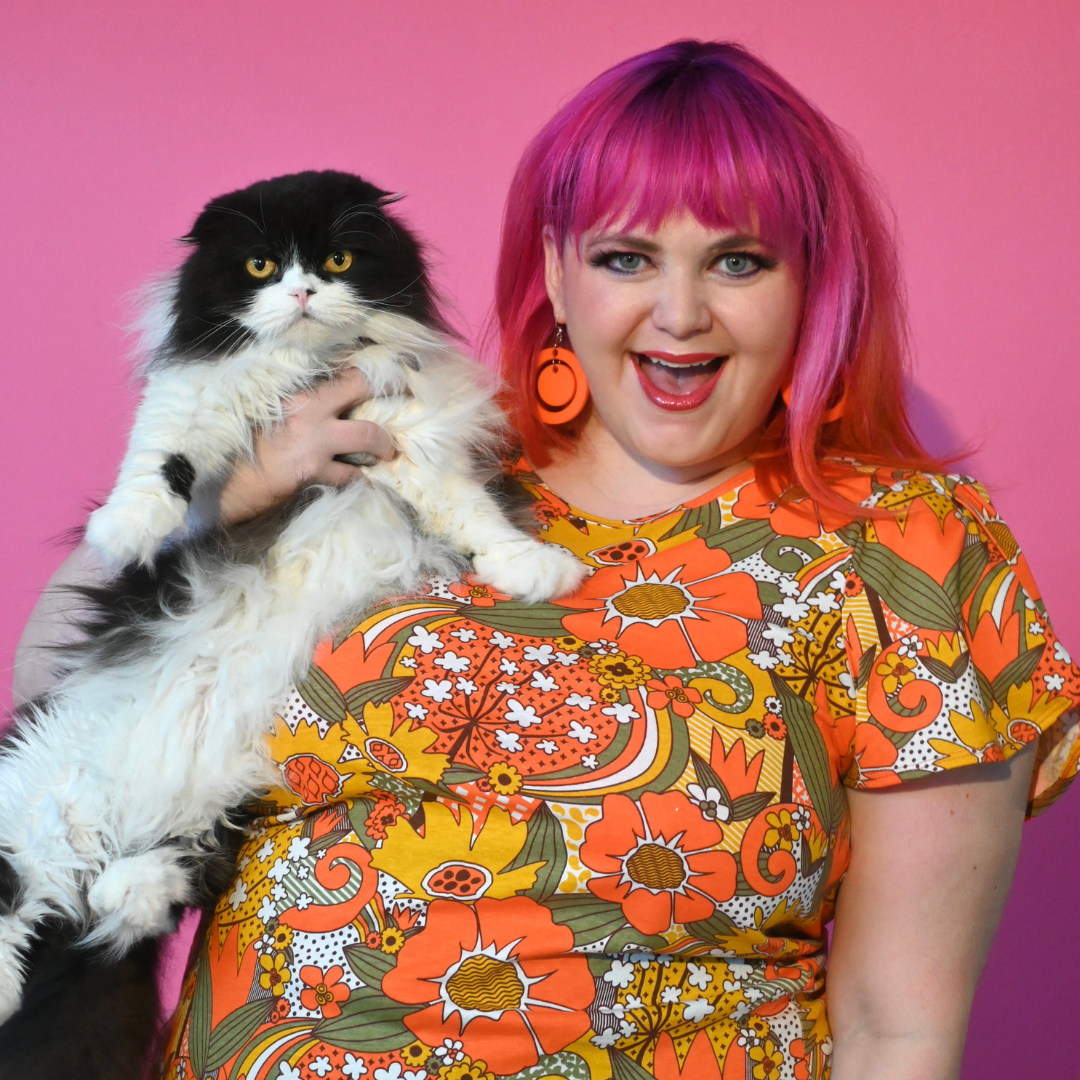 Pink-haired model with cat wearing fun, floral shirt with various flowers and swirls