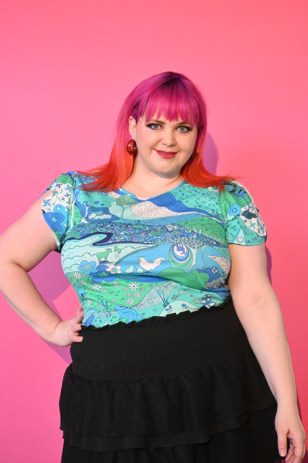 Pink haired model wearing shirt with landscape graphic in green and blue