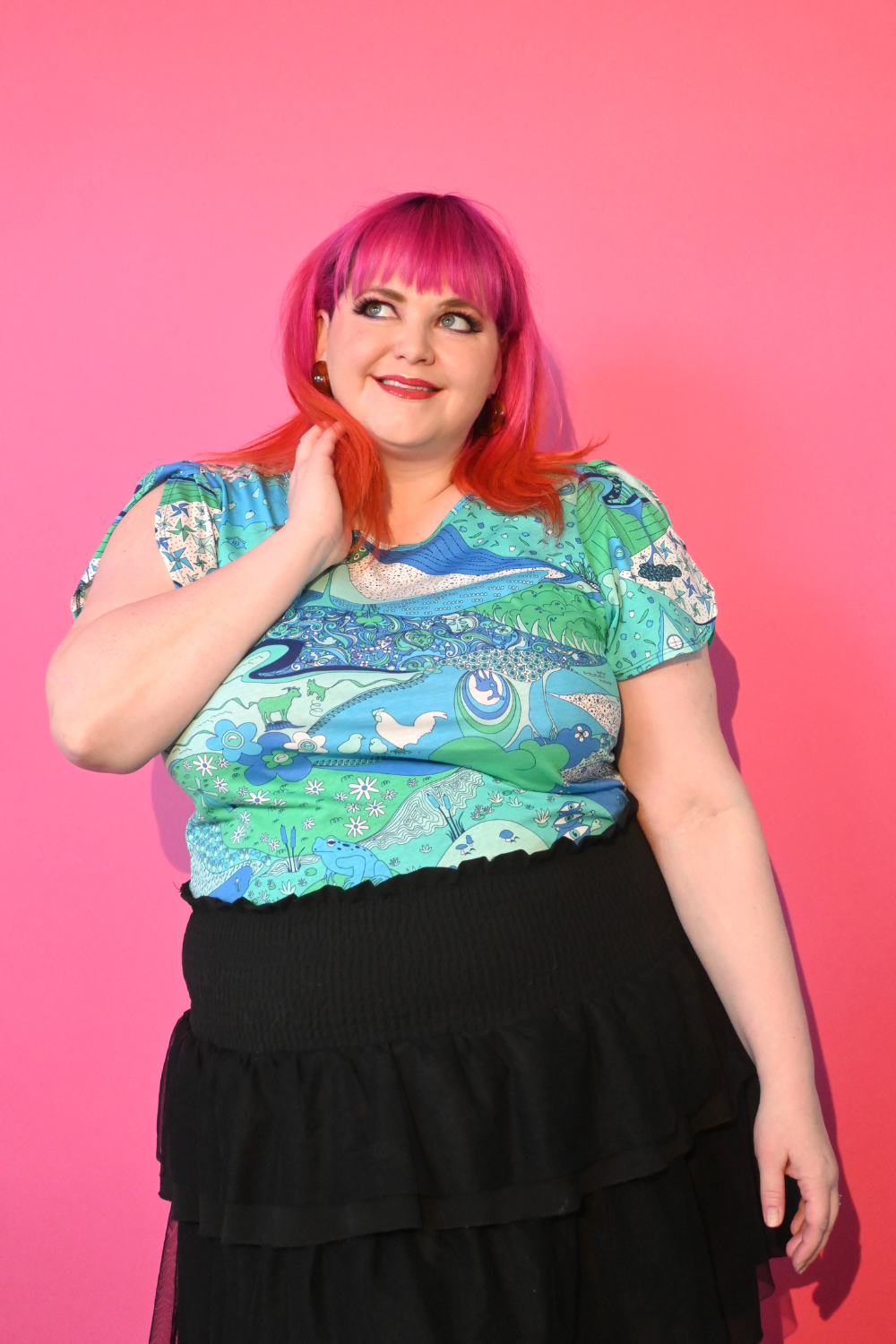 Pink haired model wearing shirt with landscape graphic in green and blue