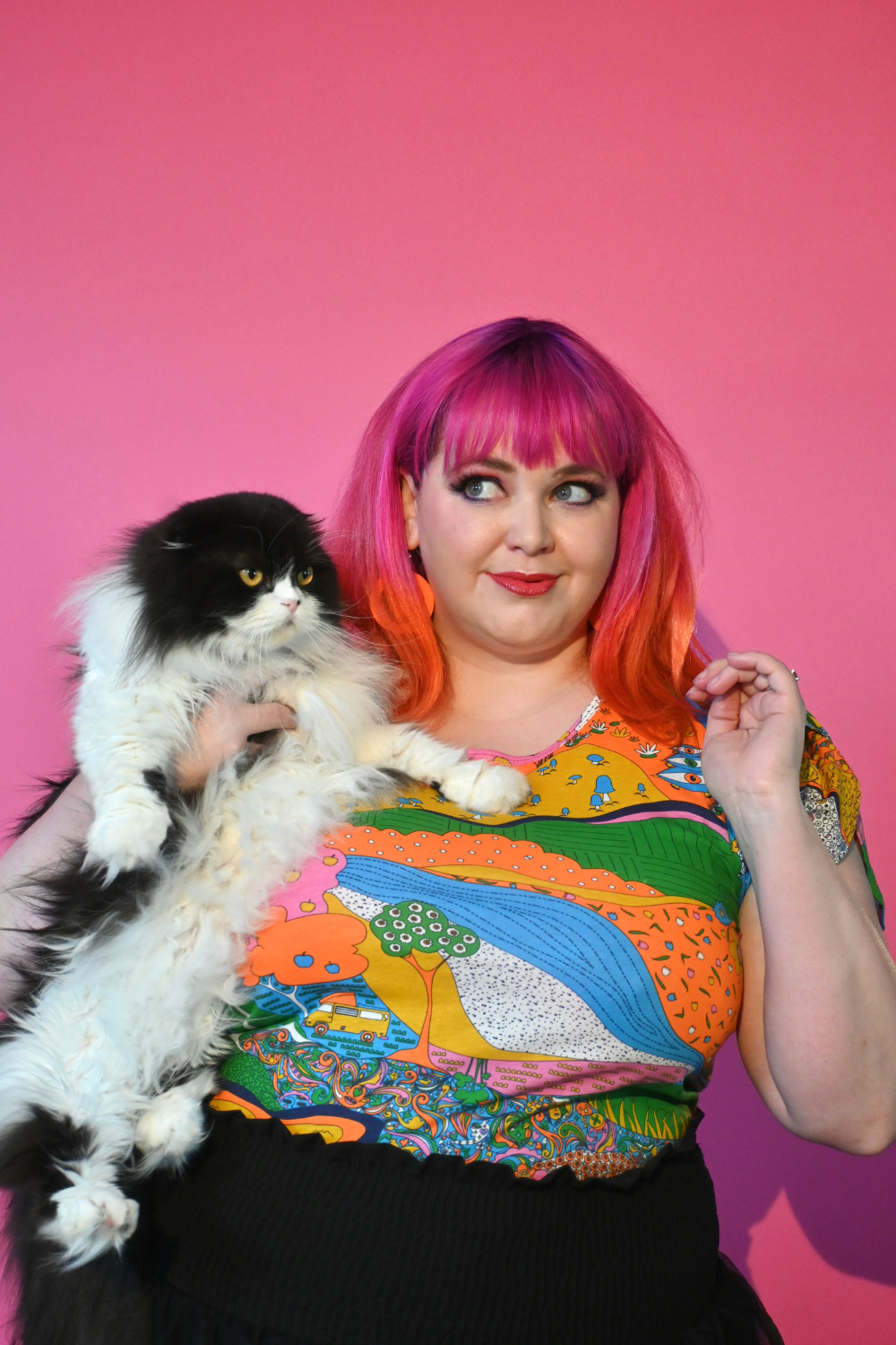 Pink haired model holding cat wearing shirt with landscape graphic in multicolor