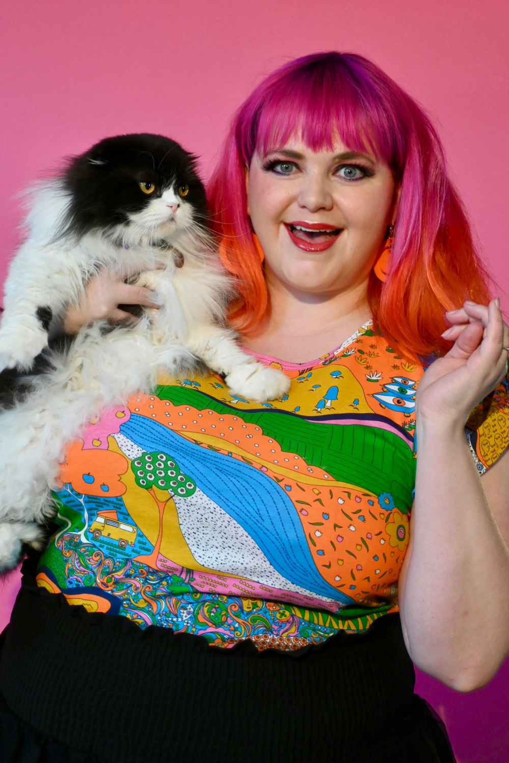Pink haired model holding cat wearing shirt with landscape graphic in multicolor