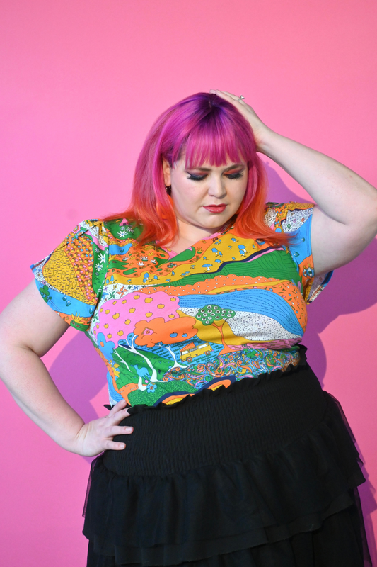 Pink haired model wearing shirt with landscape graphic in multicolor