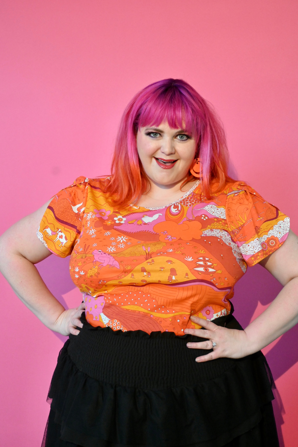 Pink haired model wearing shirt with graphic of a landscape in orange and pink