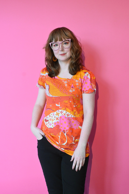 Model wearing glasses and shirt with graphic of a landscape in orange and pink