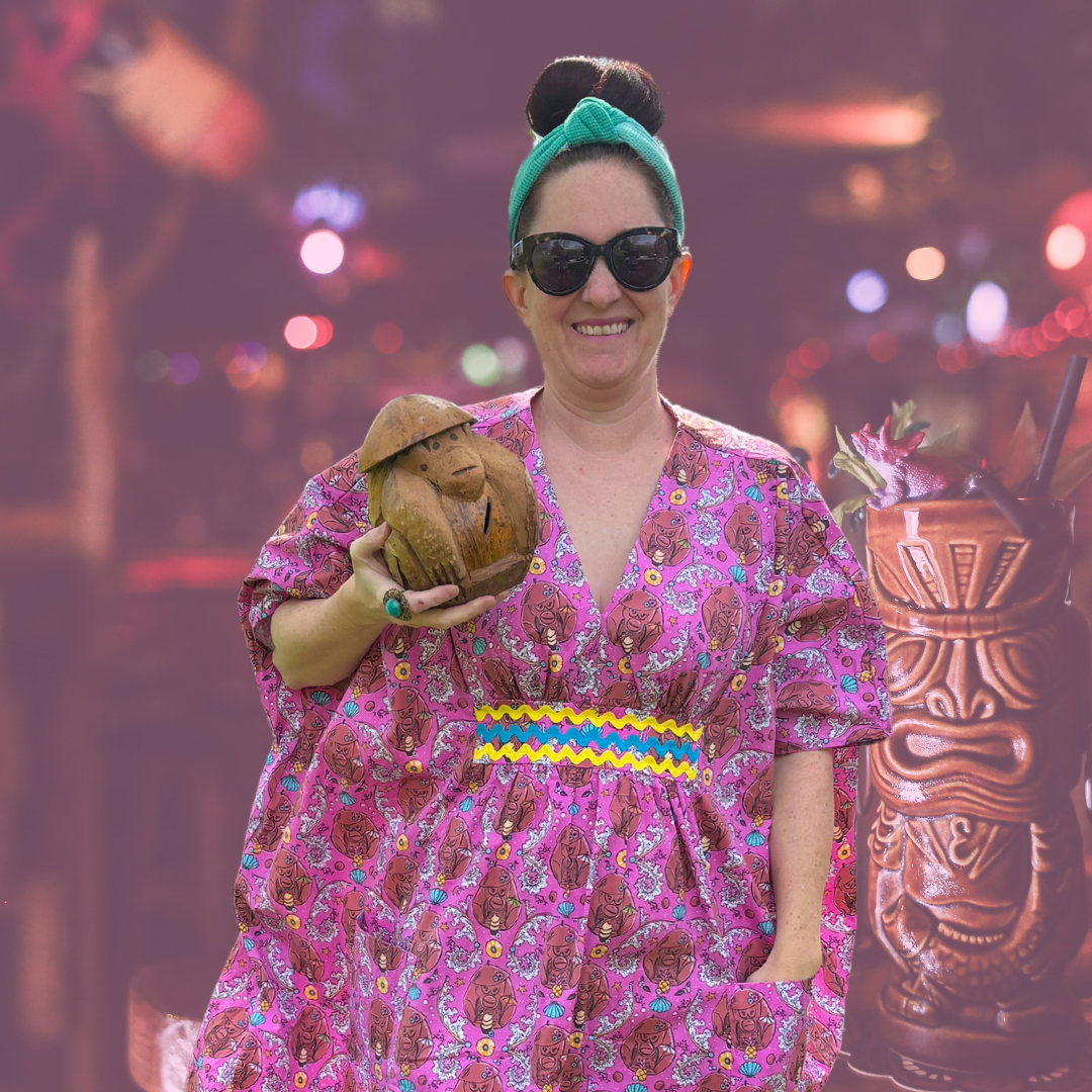 Woman holding tiki monkey, wearing monkey print caftan and tiki bar background