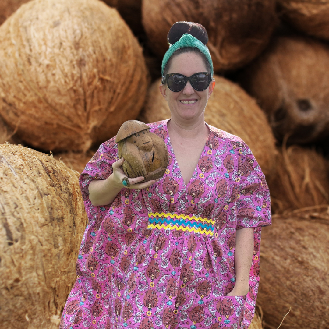 Woman with sunglasses in pink monkey print caftan with ricrac trim with coconut background