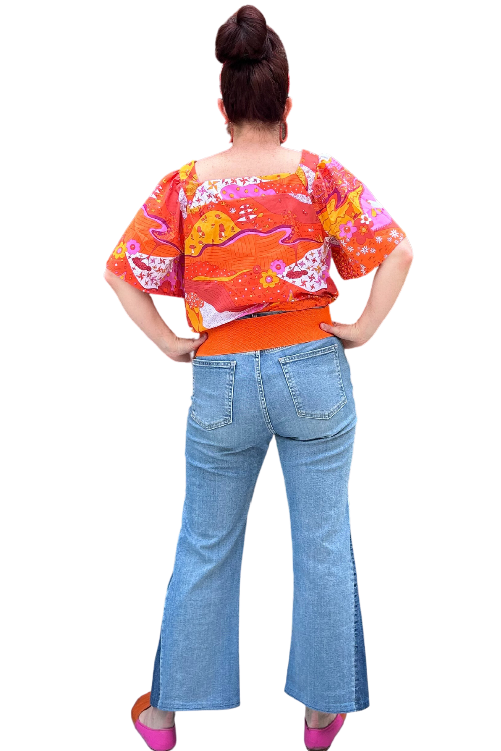 Back view of model in brightly colored woven square-neck top with landscape print in pink, orange and yellow
