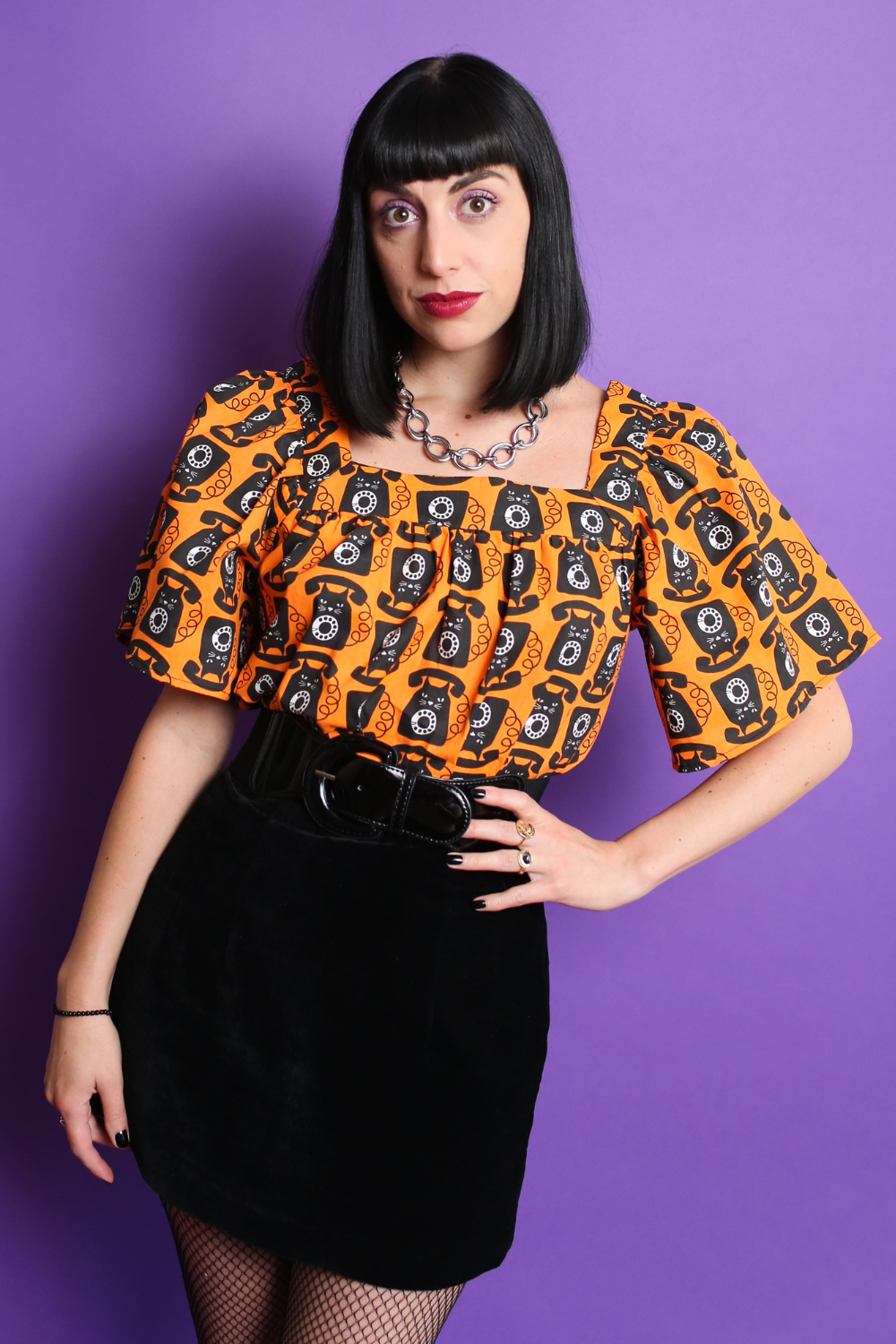 Black haired model in orange and black cat phone print top & mini skirt