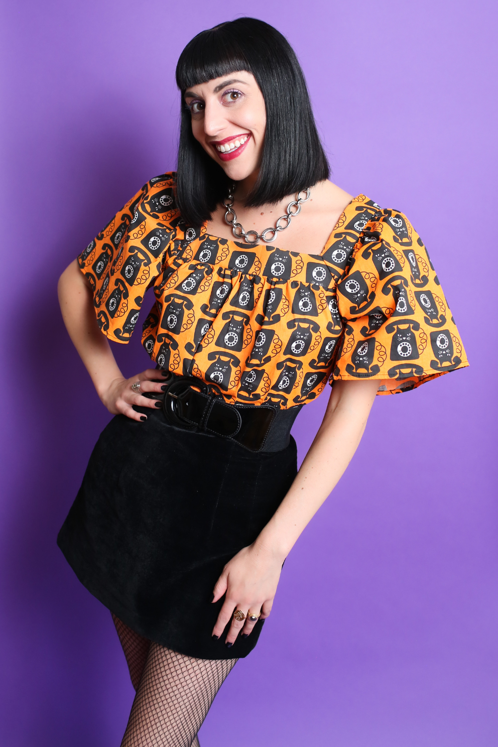 Black haired model in orange and black cat phone print top & mini skirt