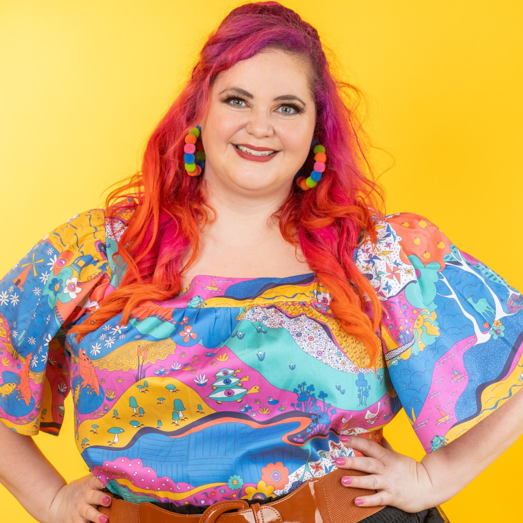 Pink-haired model wearing colorful landscape print flutter sleeve top