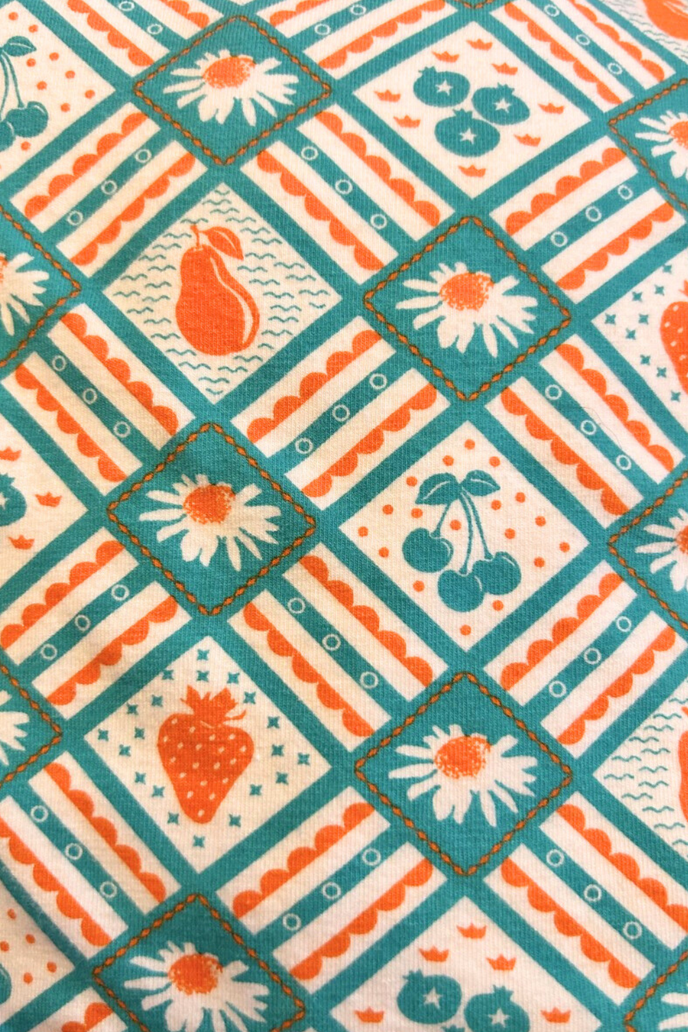 Close up of tunic in teal and orange with graphic of fruit and flowers