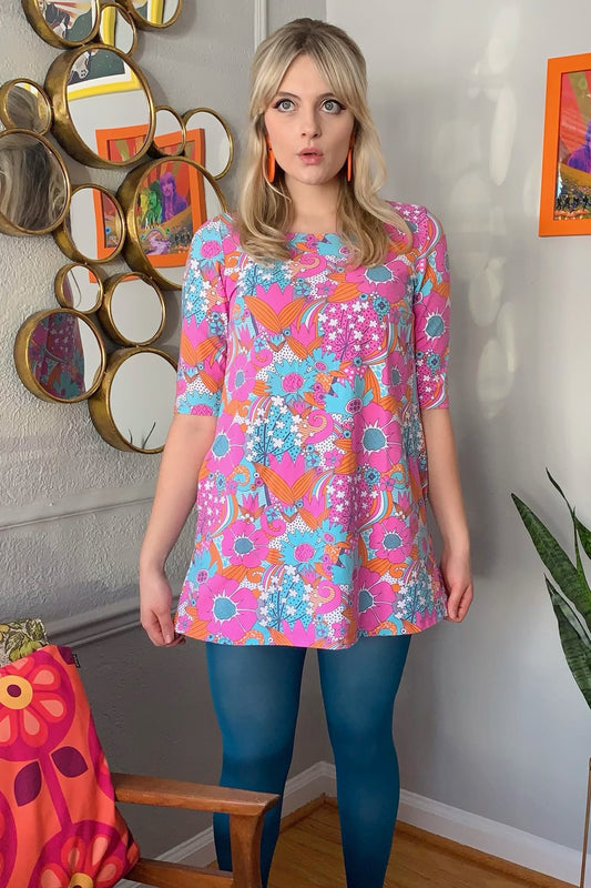 Bright pink, orange and aqua retro floral print a-line pocket tunic on blonde model in cute house