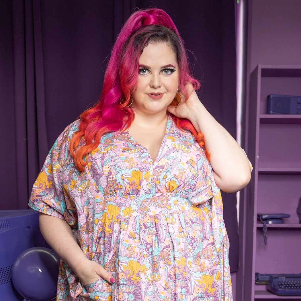 Closeup of pink, aqua and yellow v-neck mushroom, flower and snail print maxi caftan on pink-haired model