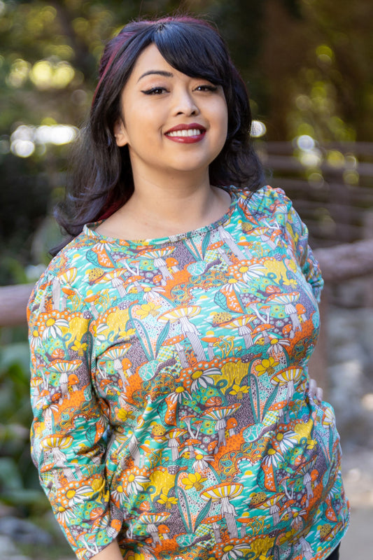 Model wearing 3/4 sleeve shirt featuring colorful fantasy landscape and mushrooms