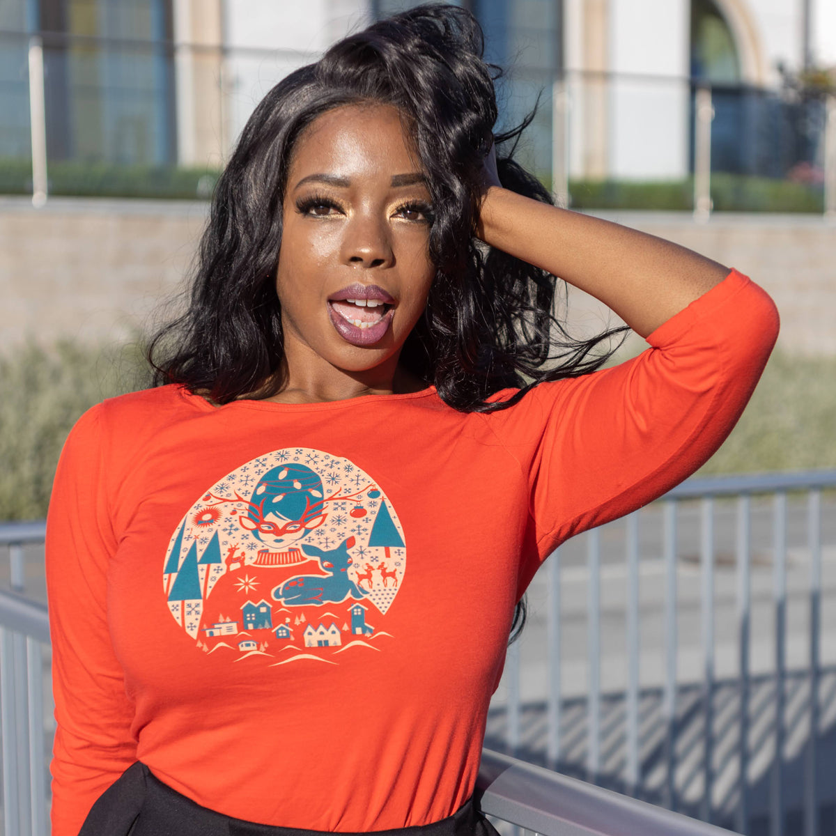 Bright red 3/4 sleeve Christmas tee with print of festive girl with beehive hair, reindeer, putz houses, snowflakes and pine trees