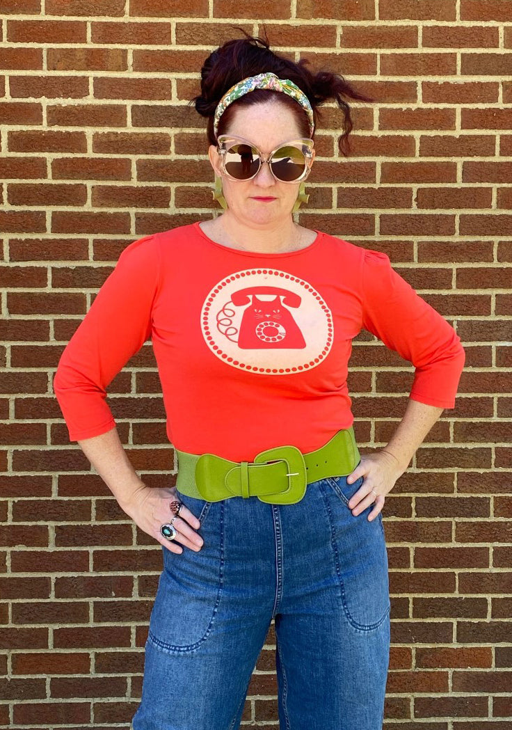 Bright red 3/4 sleeve graphic tee with rotary dial cat phone print surrounded by a circle, on woman in sunglasses