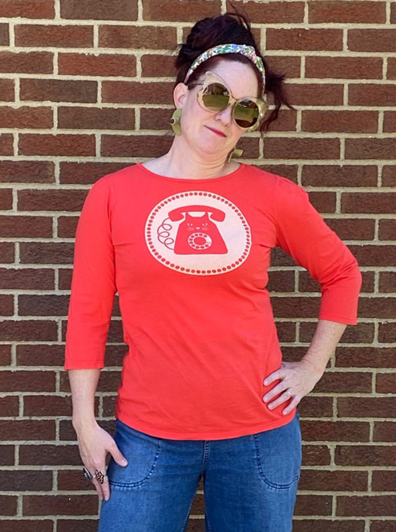 Bright red 3/4 sleeve graphic tee with rotary dial cat phone print surrounded by a circle, on woman in sunglasses