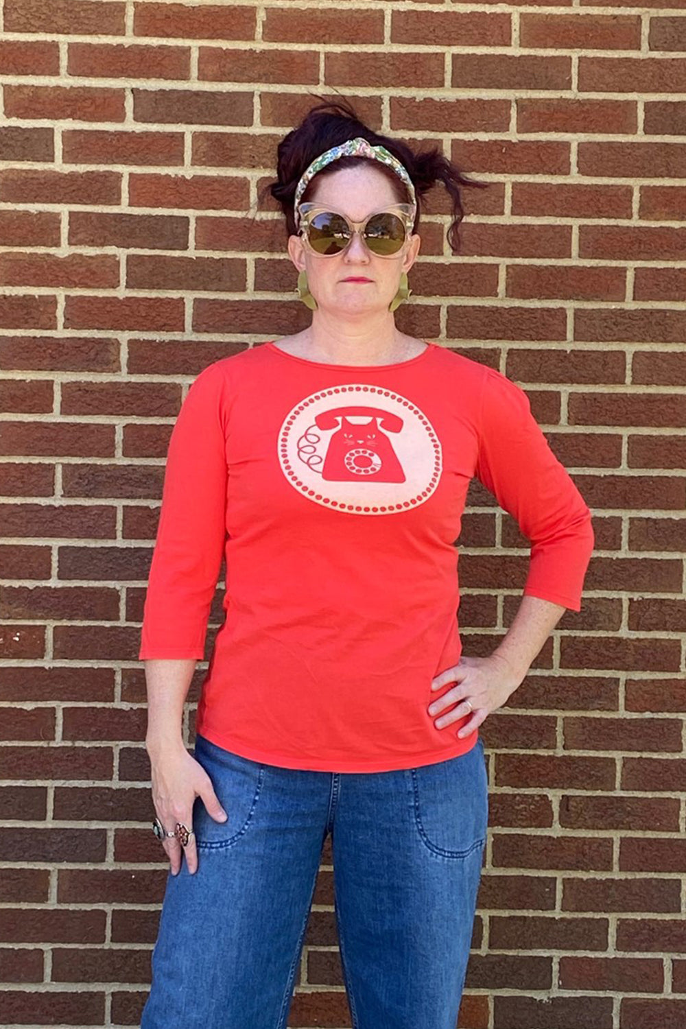 Bright red 3/4 sleeve graphic tee with rotary dial cat phone print surrounded by a circle, on woman in sunglasses