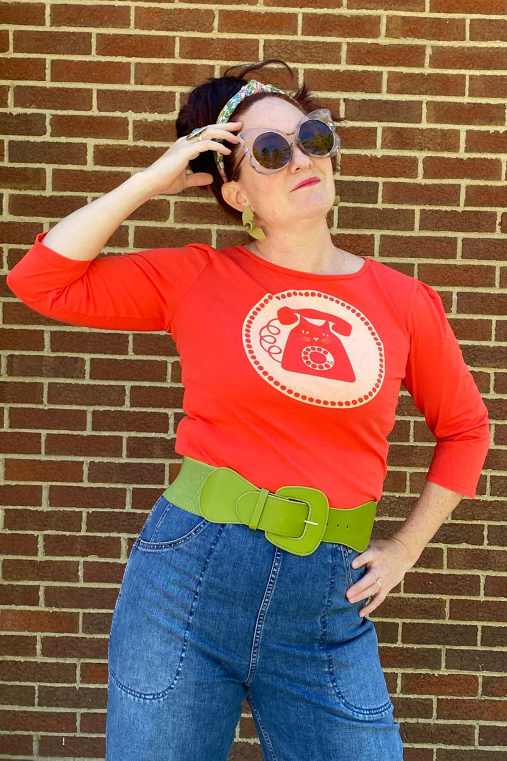 Bright red 3/4 sleeve graphic tee with rotary dial cat phone print surrounded by a circle, on woman in sunglasses