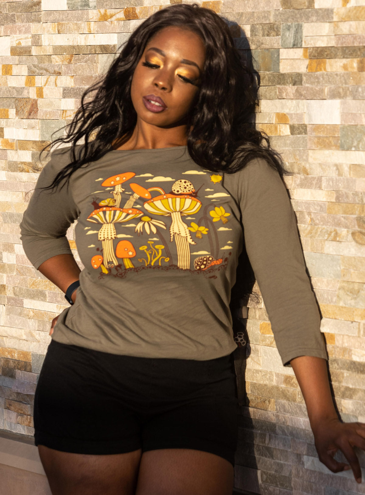 Long-haired model in olive green 3/4 sleeve tee with mushrooms, snails and flowers